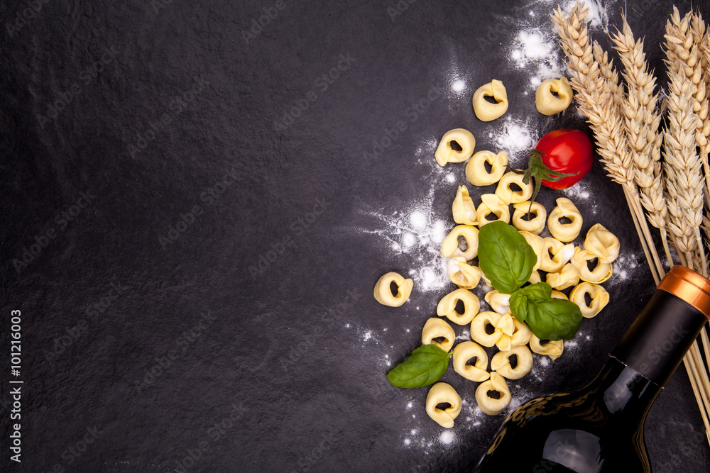 Tortellini and flour on a black stone plate.
