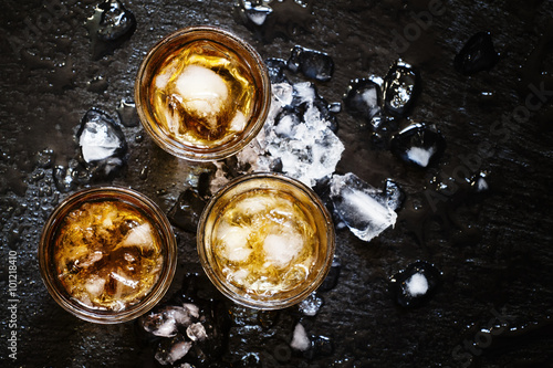 Cold whiskey in a glass with crushed ice on a black stone wet ba