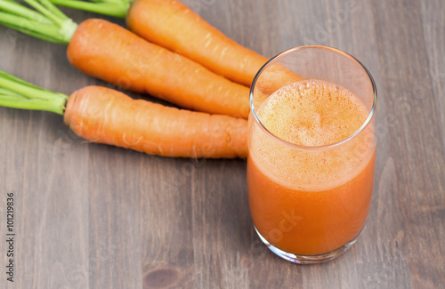 Healthy carrot smoothie in a glass and raw carrots on a wooden background