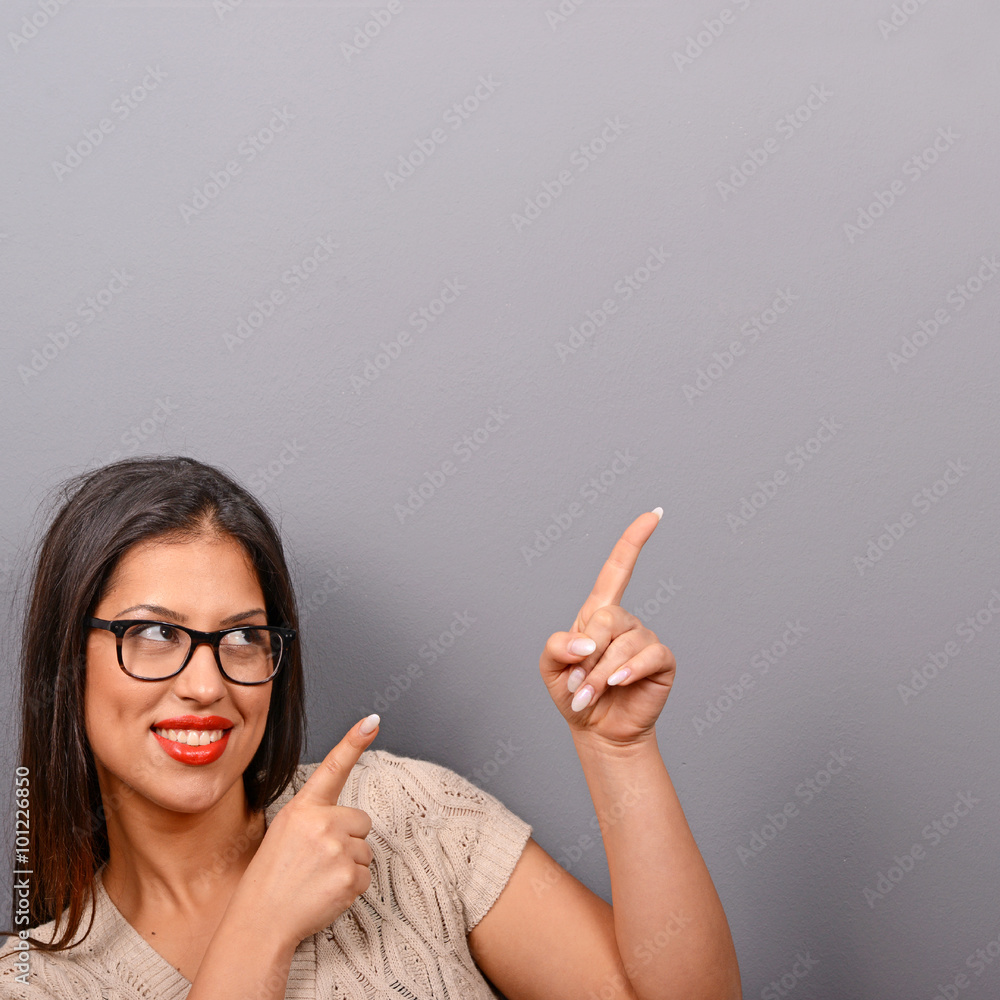 Beautiful woman pointing to blank area against gray background Beautiful woman pointing to blank area against gray background