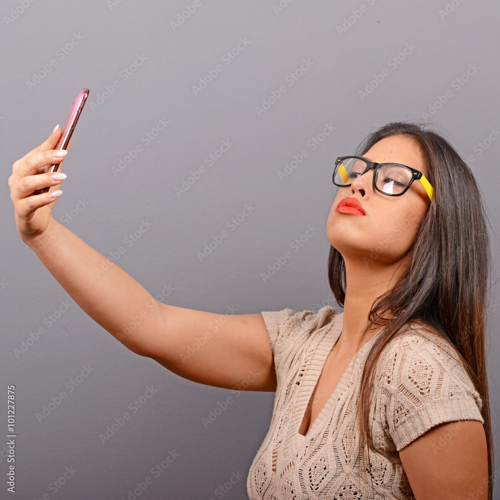 Portrait of a girl taking selfie with cellphone against gray bac Portrait of a girl taking selfie with cellphone against gray bac
