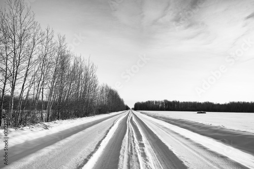 Vehicle tracks through deep snow on a rural backroad in black and white winter landscpe