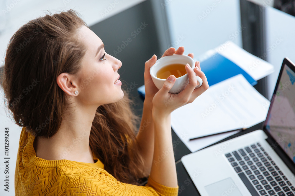 Woman sitting at the table with laptop and drinking tea