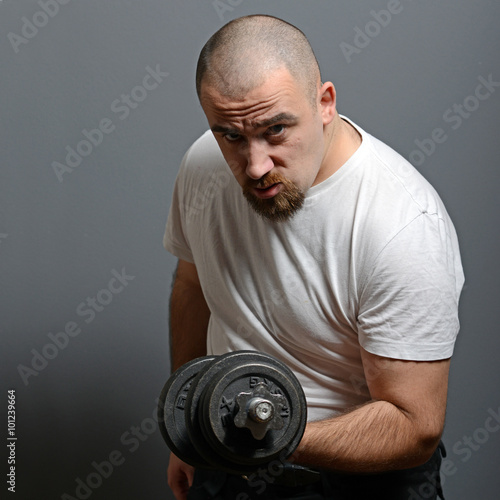 Portrait of a funny man holding dumbbells against gray backgroun