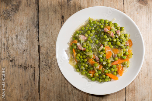 Petit pois a la Francaise looking down on plate. A traditional popular French dish prepared with garden peas, carrots, bacon, leek, onion and braised lettuce
