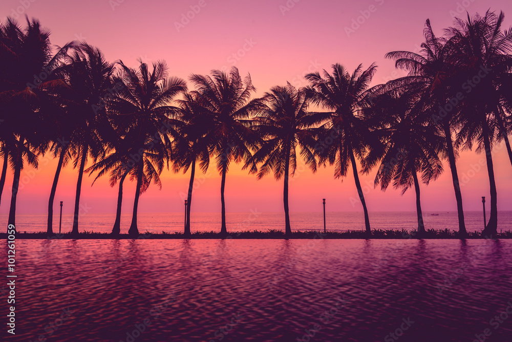 Sunset time with coconut palm trees silhouette near outdoor swimming pool in hotel and resort. Summer travel vacation concept