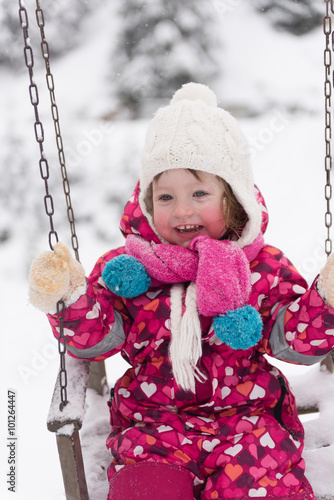 little girl at snowy winter day swing in park