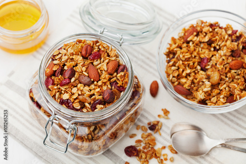 Homemade granola in jar on white table, healthy breakfast of oatmeal muesli, nuts, seeds and dried fruit