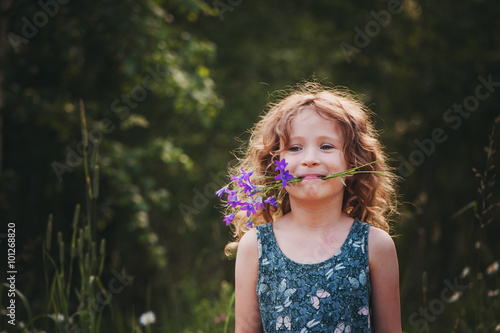 Happy child girl playing with bouquet of bluebells in summer. Happy childhood  outdoor activities. Exploring nature and picking flowers. Cozy country vacations.