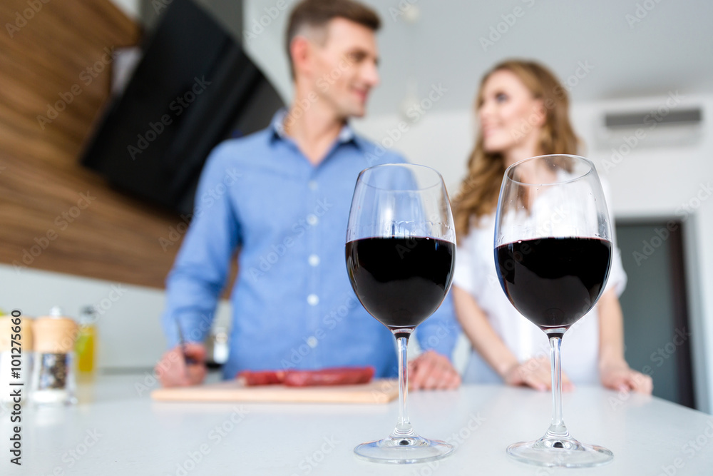 Two glasses of wine and happy couple standing on kitchen