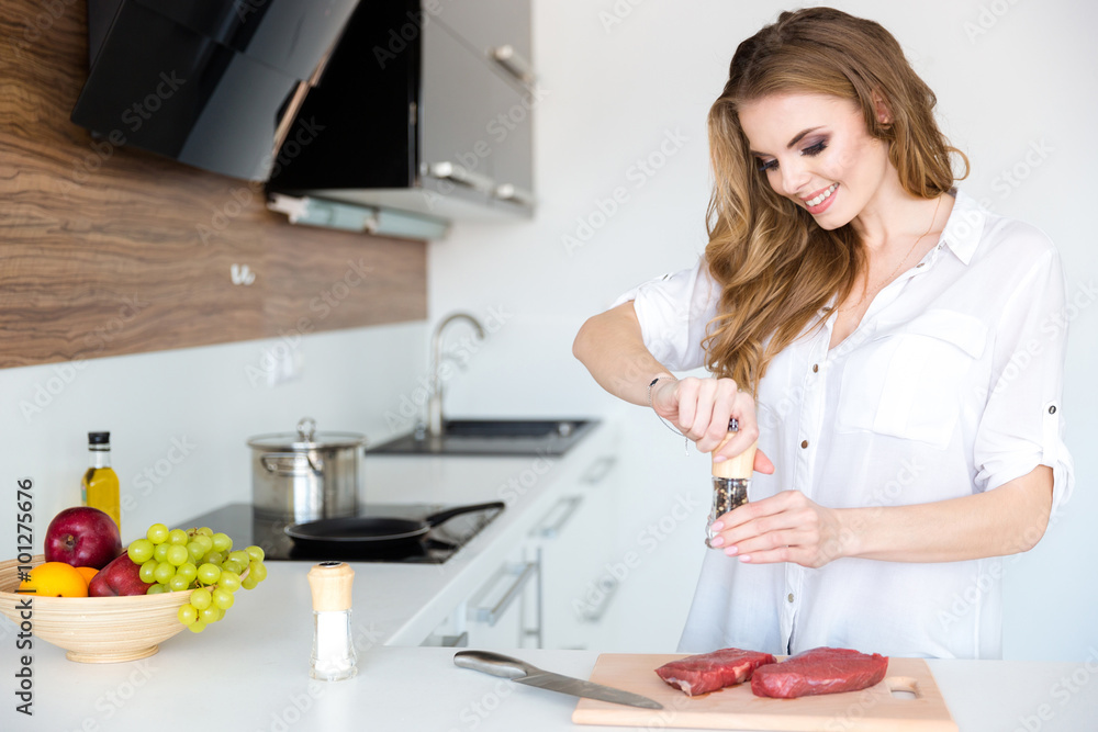 Happy beautiful young woman cooking meat on the kitchen