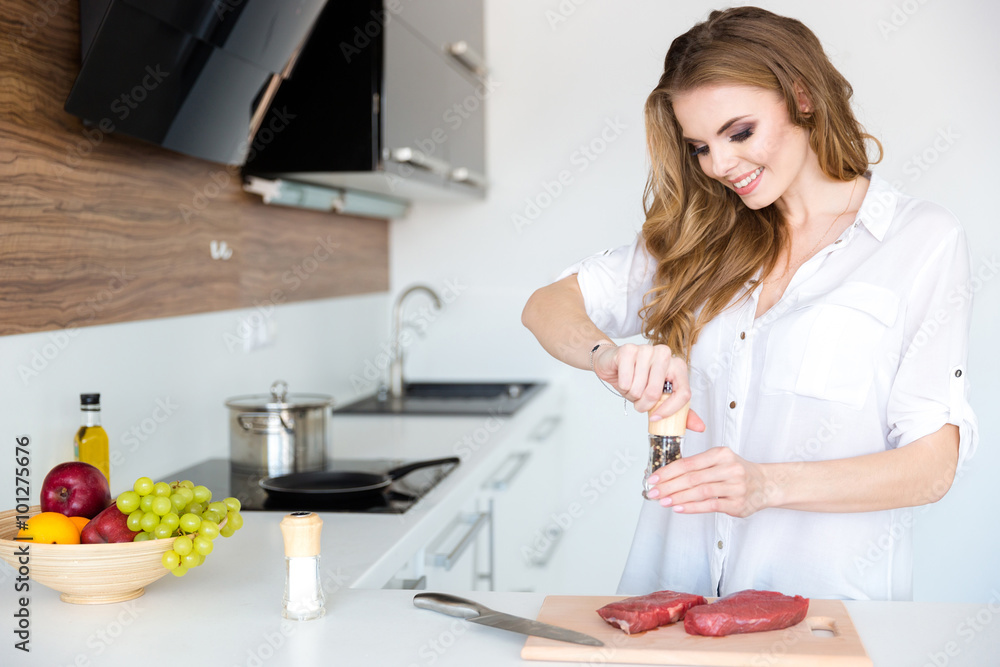 Happy beautiful young woman cooking meat on the kitchen Happy beautiful young woman cooking meat on the kitchen