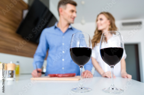 Two glasses of wine and happy couple standing on kitchen
