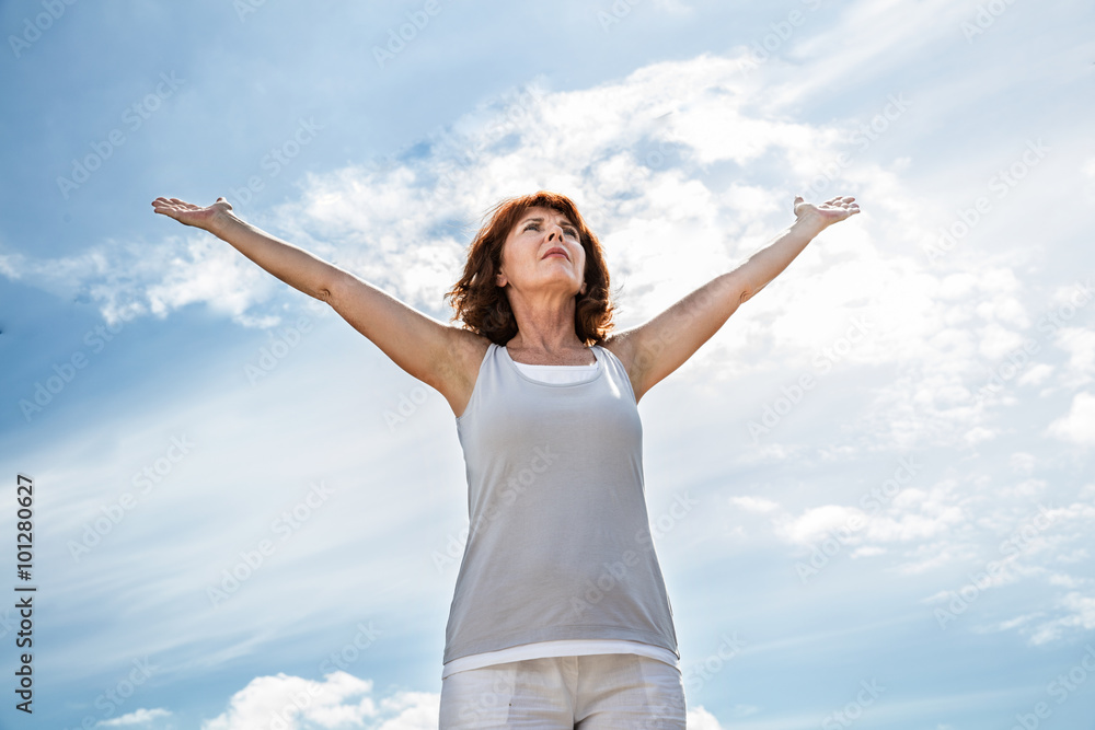 breathing outside - older yoga woman opening up her arms to exercise,practicing meditation for freedom over summer blue sky,low angle view. breathing outside - older yoga woman opening up her arms to exercise,practicing meditation for freedom over summer blue sky,low angle view.