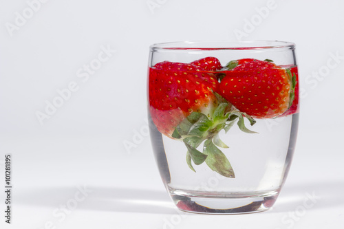 Water glass with floating strawberries, with blank space at left