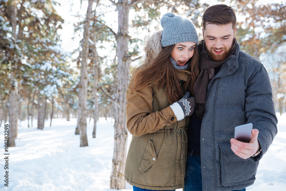 Couple using smartphone in winter park Couple using smartphone in winter park