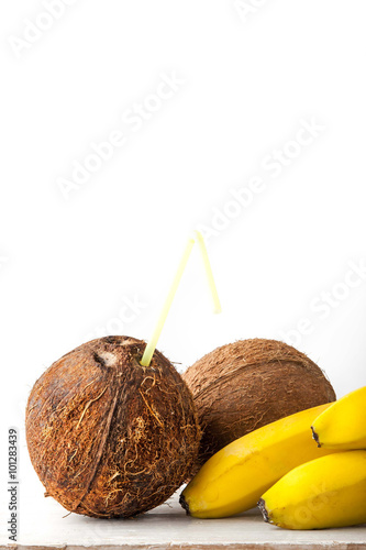 Coconut with straw and bananas on the white table vertical