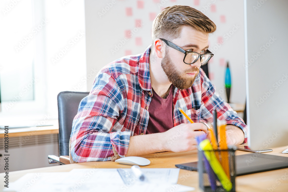 Serious man sitting on workplace and looking over glasses Serious man sitting on workplace and looking over glasses