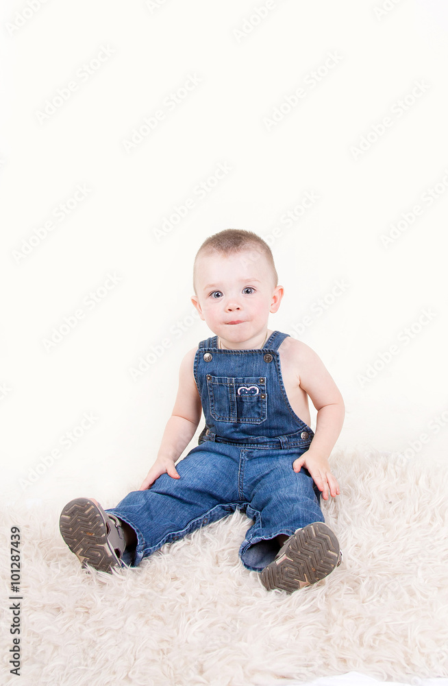 Cute baby with big blue eyes in denim overalls sitting isolated on white background. Cute baby with big blue eyes in denim overalls sitting isolated on white background.
