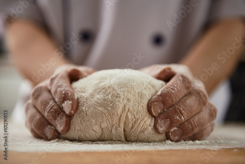 Woman chef with raw dough. Young female in uniform preparing bread dough on wooden table.  photo