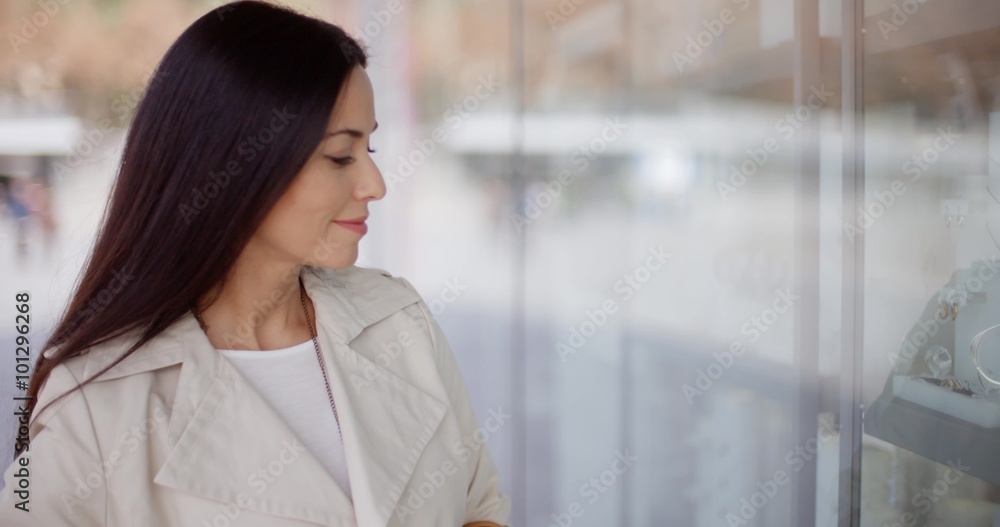 Laughing vivacious attractive young woman standing outside a store window in a town street grinning at the camera Laughing vivacious attractive young woman standing outside a store window in a town street grinning at the camera