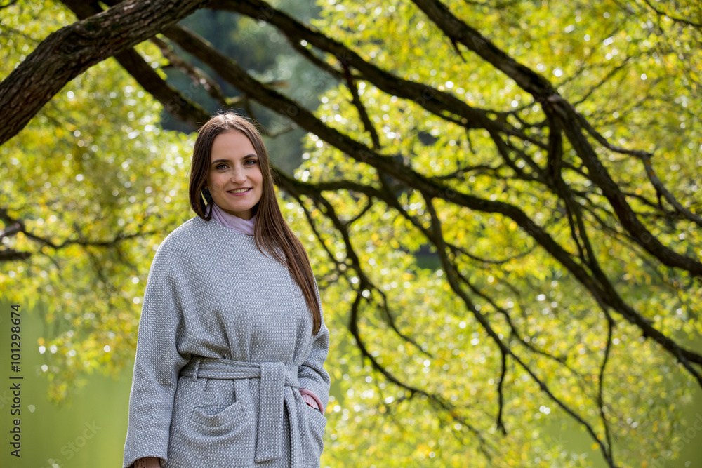 Attractive young woman enjoying her time outside in park next to the tree. Walking with happy smile. Healthy lifestyle Attractive young woman enjoying her time outside in park next to the tree. Walking with happy smile. Healthy lifestyle