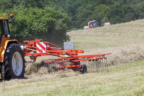 Canvas Print Farmer using a rotary rake to turn drying grass for hay and fodder for livestock