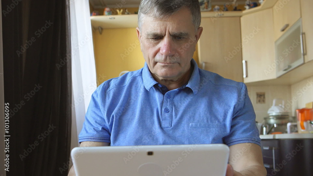 Portrait of a senior man at the blue shirt sits and types a tablet PC at home
Portrait of a senior man at the blue shirt sits and types a tablet PC at home