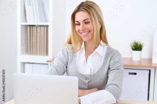 Portrait of young business woman sitting at the desk on office background