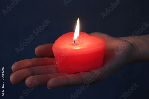 Red Heart candle in a hand. Light in the dark