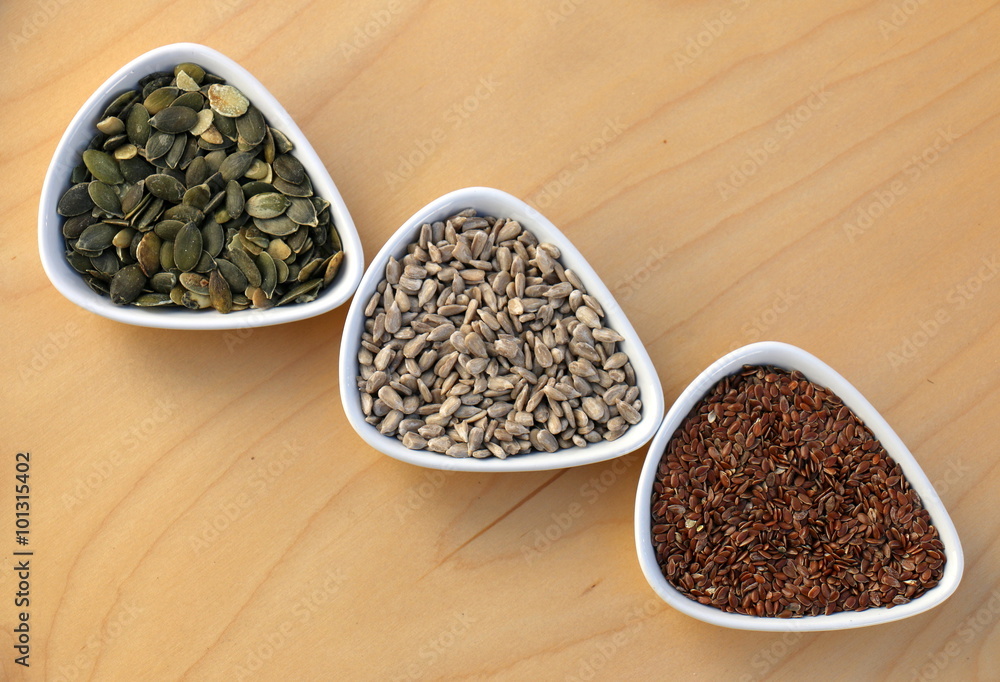 Eatable seeds (sunflower, pumpkin, flax) in three bowls arranged in an arrow