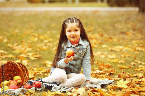 Beautiful little girl with basket of apples sitting on plaid  outdoor