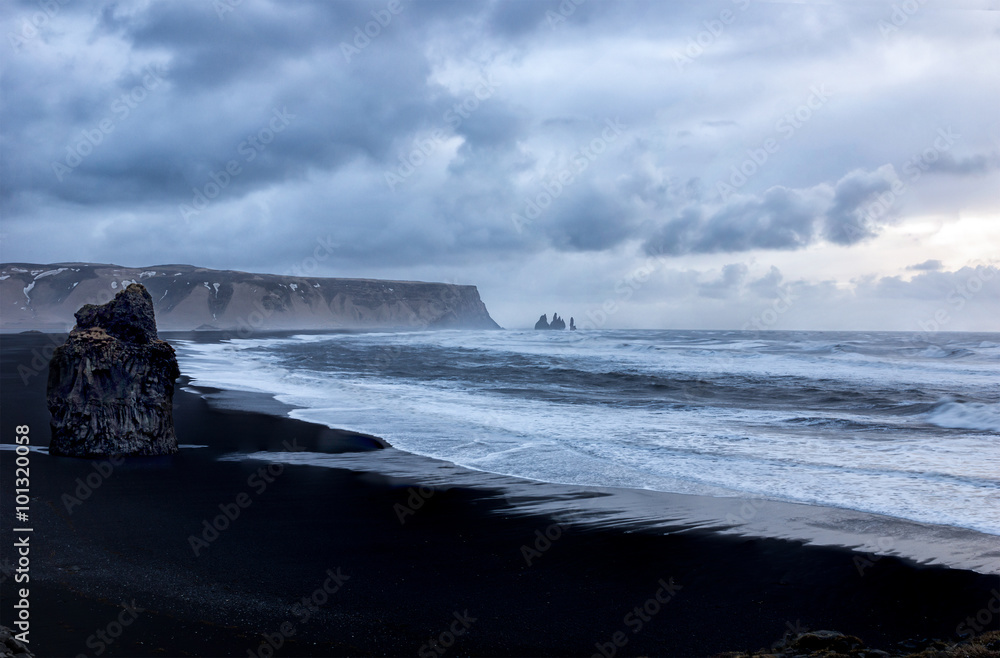 Storm clouds over Black sand beach in Vik Iceland, with rock formation on the beach and the famous  Reynisfjara rocks in the background