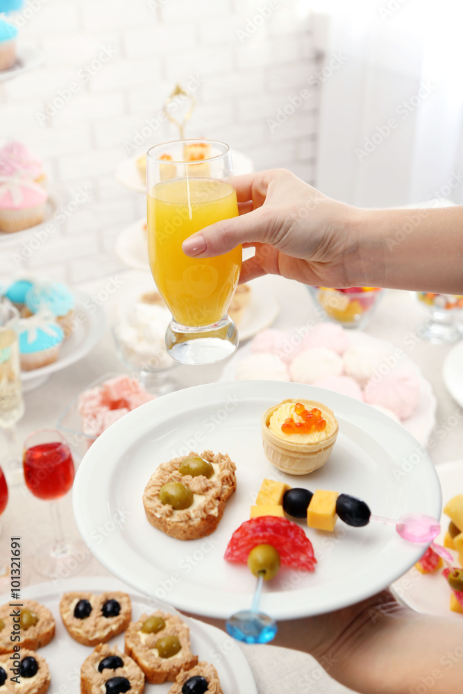 Woman holding glass of juice and plate with snacks on buffet background Woman holding glass of juice and plate with snacks on buffet background
