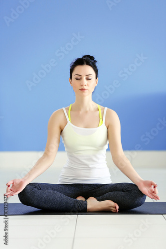 Health concept. Young attractive woman does yoga exercise in the room against blue wall