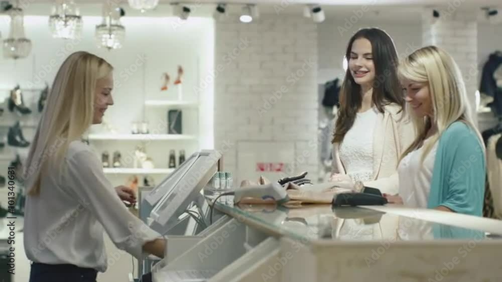 Two cheerful girls are checking out at a cash desk in a department store. Shot on RED Cinema Camera. Two cheerful girls are checking out at a cash desk in a department store. Shot on RED Cinema Camera.