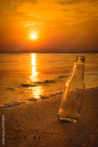 Glass bottle on the sand at sunset.