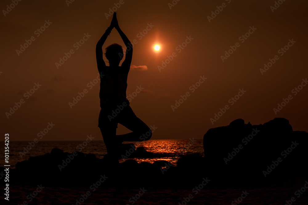 man silhouette in yoga pose against sun disk over sea