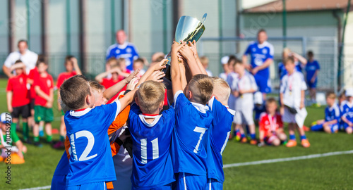 Young Sport Team with Trophy. Boys Celebrating Sports Achievement. Young Soccer Players Holding Trophy. Celebrating Soccer Football Championship. Winning team of sport tournament for kids children.