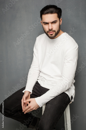 sexy fashion man model in white sweater, jeans and boots posing dramatic