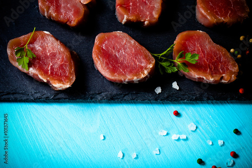 Raw meat with herbs and spices on a black slate plate on a blue