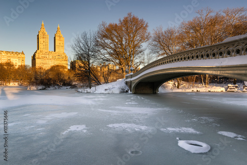 Cold Central Park winter sunrise on the frozen Lake with the Bow Bridge and Upper West Side buildings. Wintertime in Manhattan, New York City