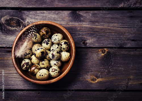 Quail eggs in a wooden bowl on a gray wooden background.