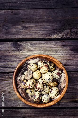Quail eggs in a wooden bowl on a gray wooden background.
