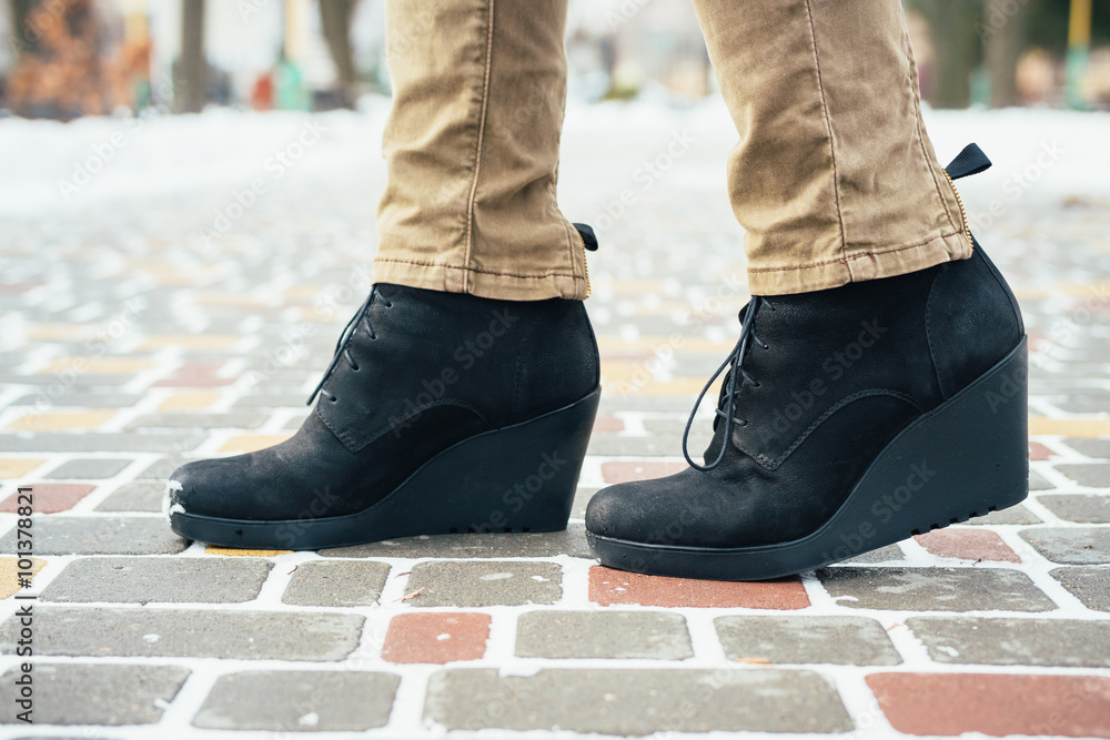 Female feet in black boots standing on the sidewalk in the winte Female feet in black boots standing on the sidewalk in the winte
