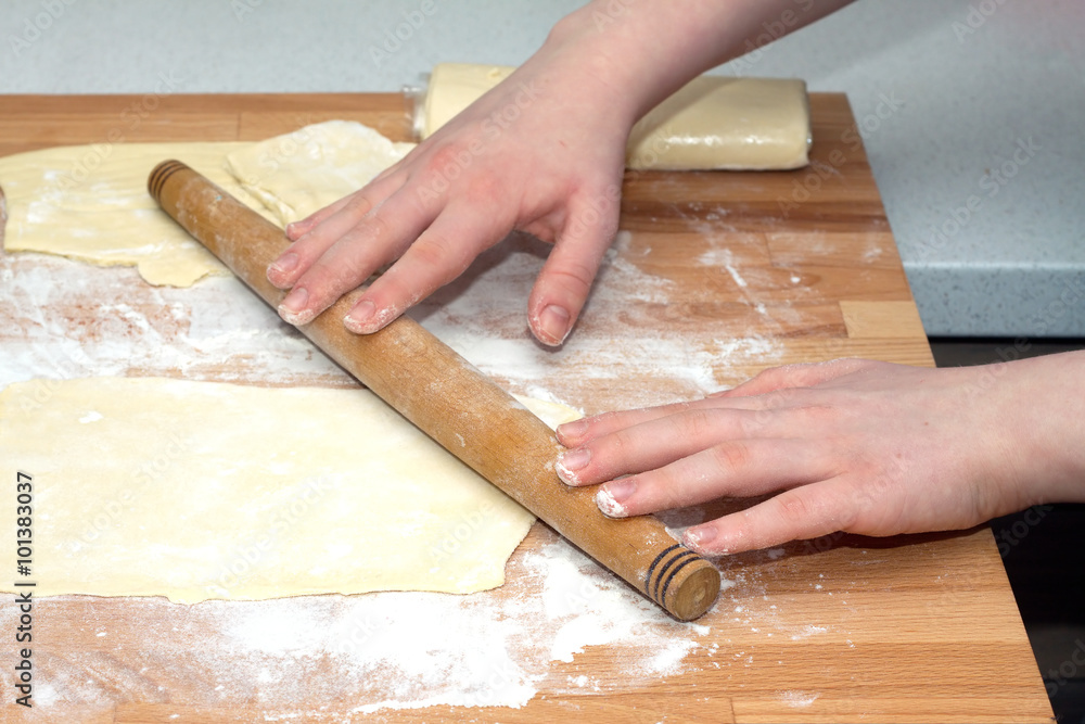 Female hands with rolling pin preparing dough for baking on brown wooden cutting board on kitchen table. Closeup view Female hands with rolling pin preparing dough for baking on brown wooden cutting board on kitchen table. Closeup view