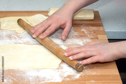 Female hands with rolling pin preparing dough for baking on brown wooden cutting board on kitchen table. Closeup view