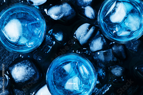 Blue cocktail with ice cubes on black stone background, top view