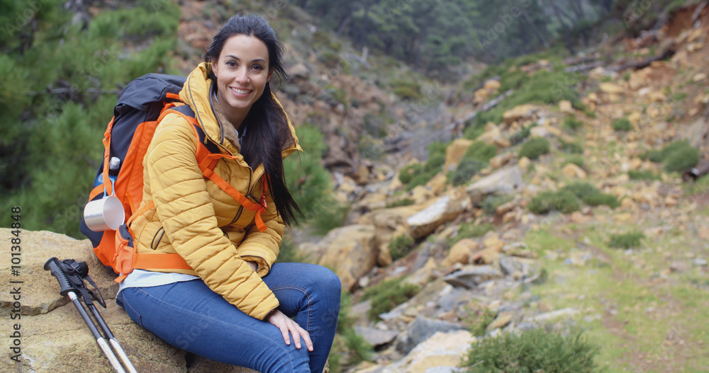 Young woman backpacker taking a break from hiking relaxing on a mountain rock in a valley to enjoy the view