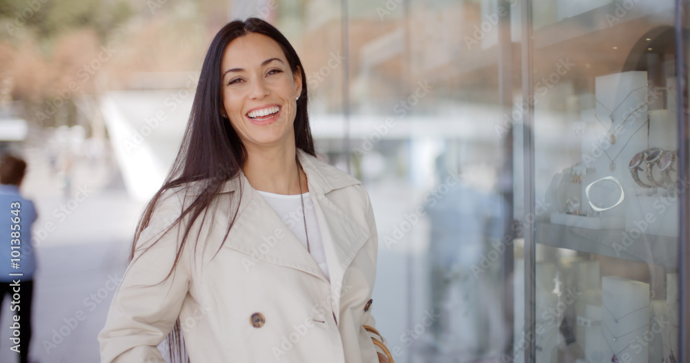 Fototapeta premium Roześmiana vivacious atrakcyjna młodej kobiety pozycja na zewnątrz sklepu okno w grodzkiej ulicie ono uśmiecha się przy kamerą